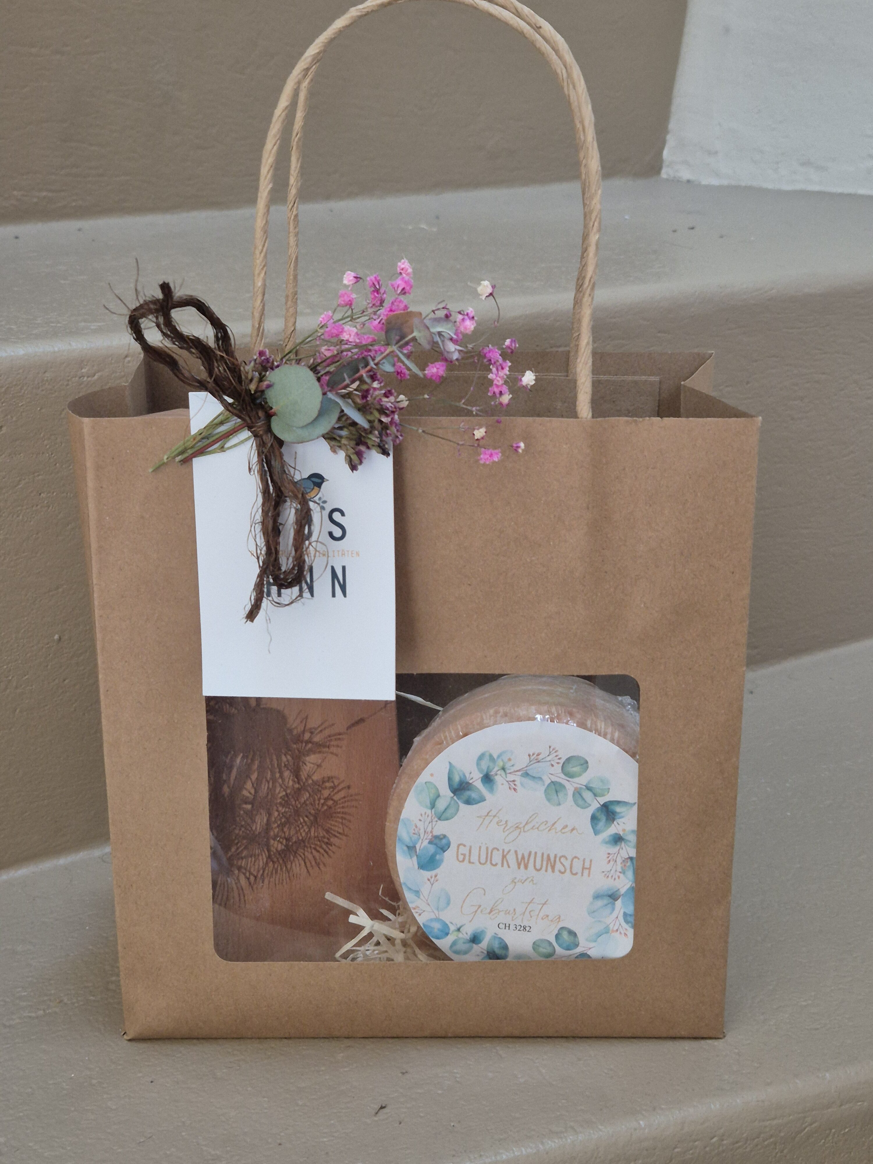 Geschenktasche mit Messerbrett und runder Käse mit Text "Herzlichen Glückwunsch zum Geburtstag"